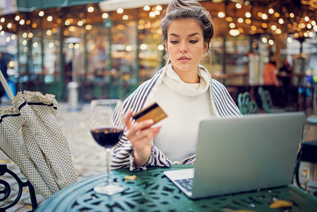 Young woman is shopping for wine online using her credit card and laptop in a rainy day